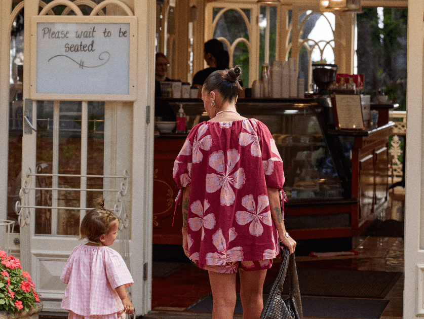 Women in maroon coloured set walking into a cafe with her toddler