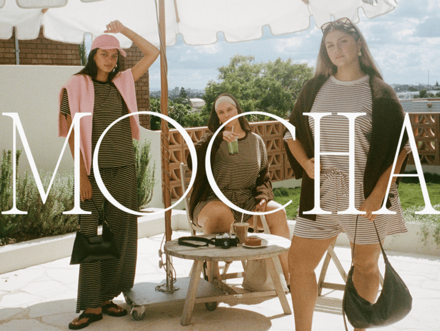 three girls in floral autumn outfits from the lullaby club merlot bloom collection wine colour set, gold vest, floral pants, florla set, headband drinking wine in green marble bend rattan chair and crazy pave tile kitchen