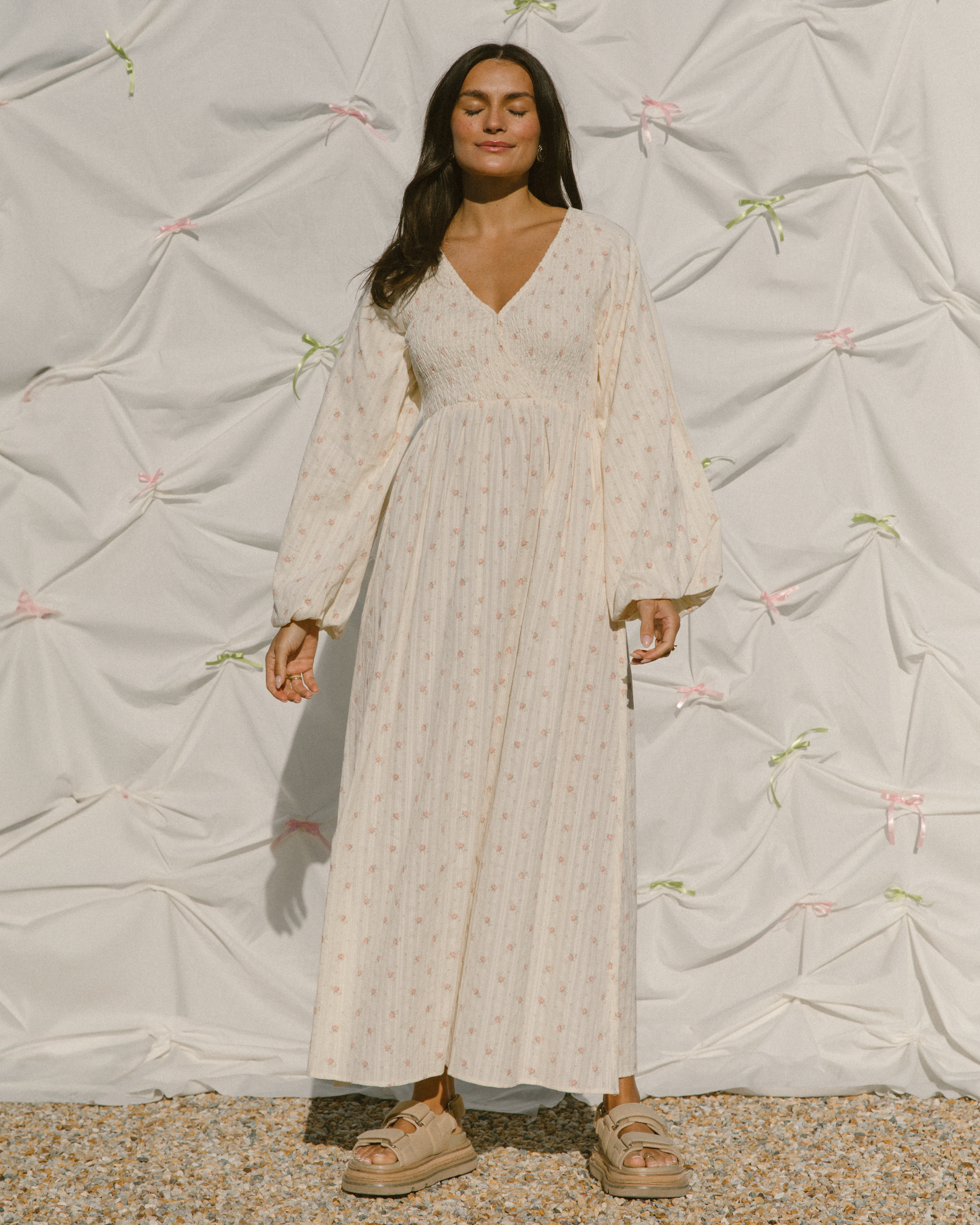 Woman wearing cream coloured long sleeved maxi dress with delicate pink flower print.