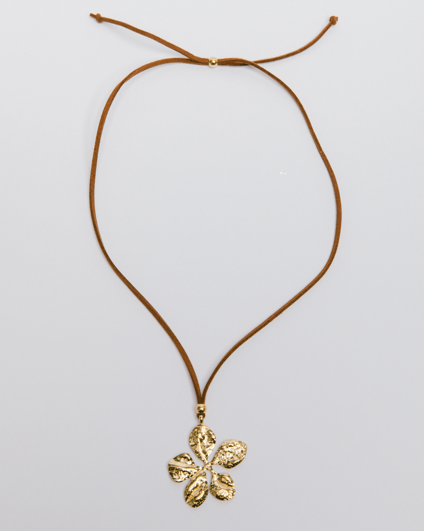 Gold flower pendant on a brown cord against a light gray background