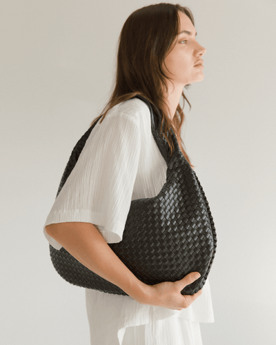 Woman holding a woven black bag against a plain background