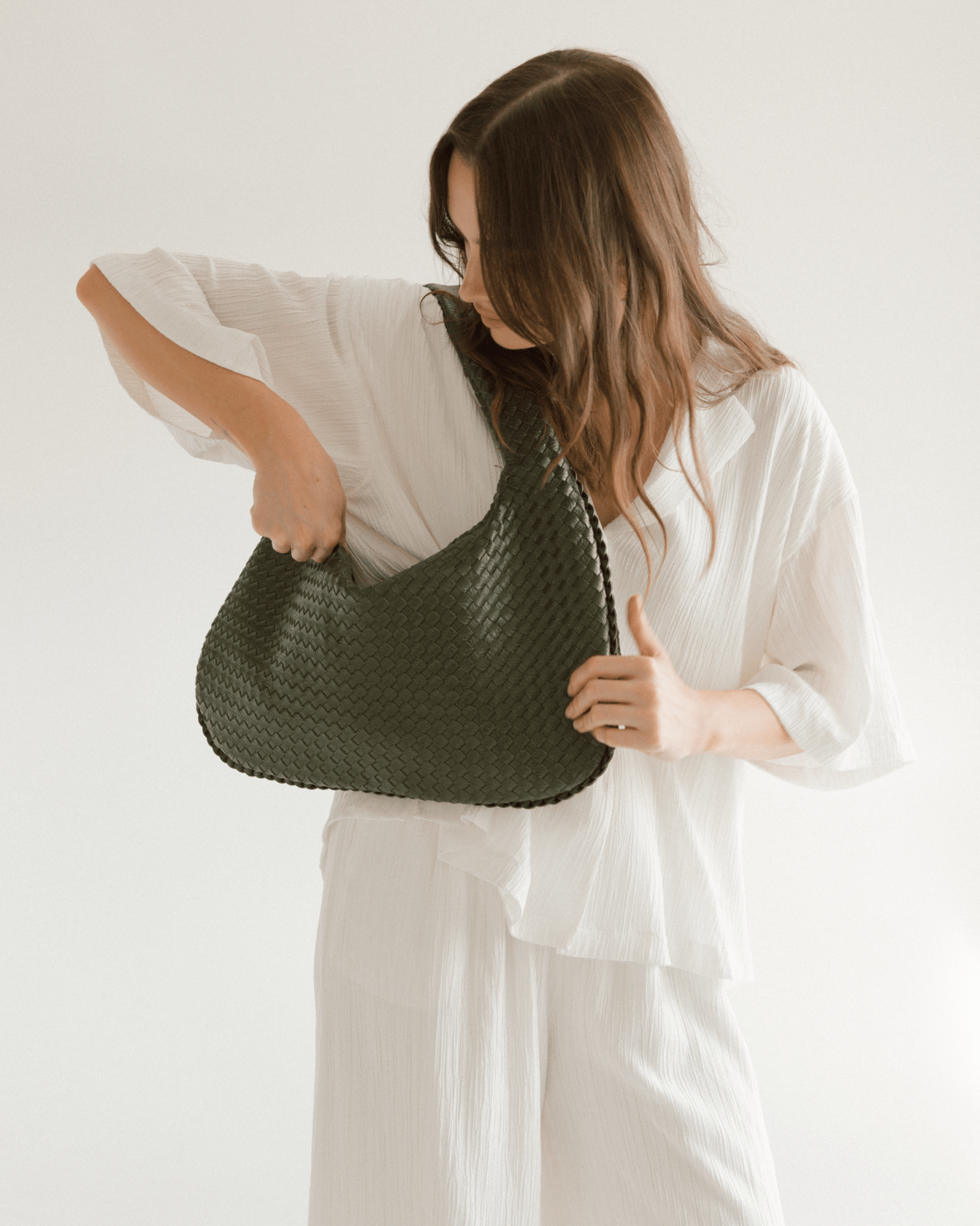 Woman holding a green woven handbag against a plain background