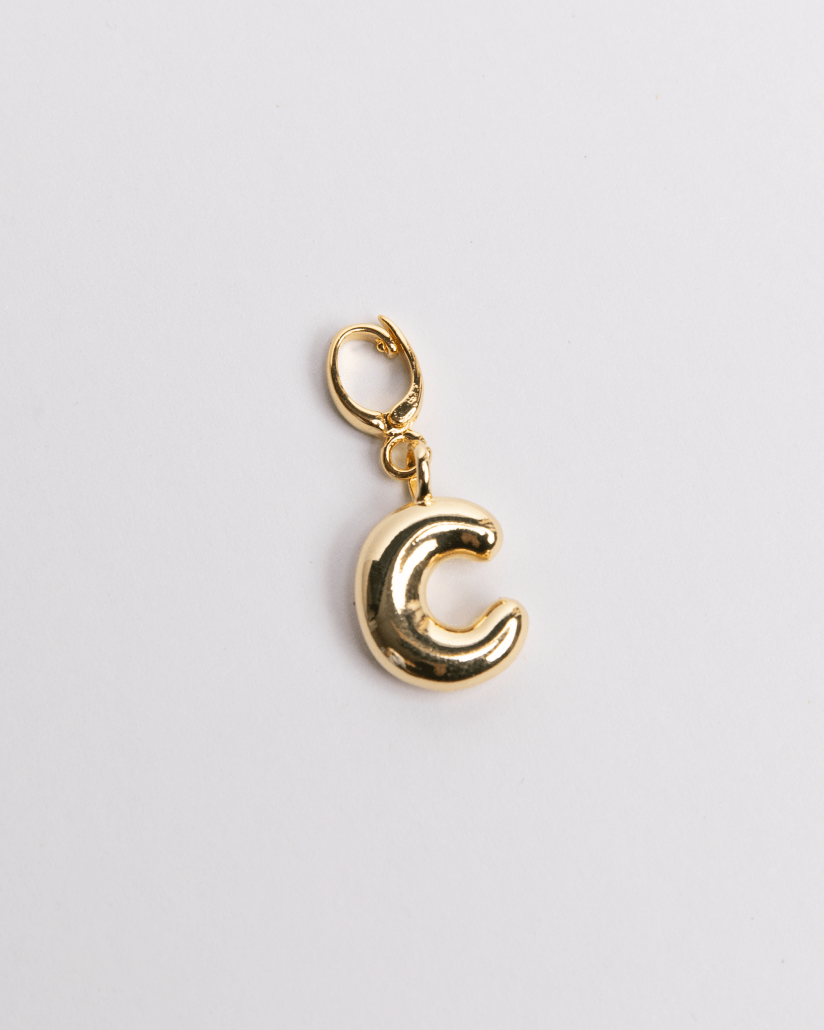 A gold-colored charm in the shape of the letter 'C' with a clasp for attaching to jewelry.