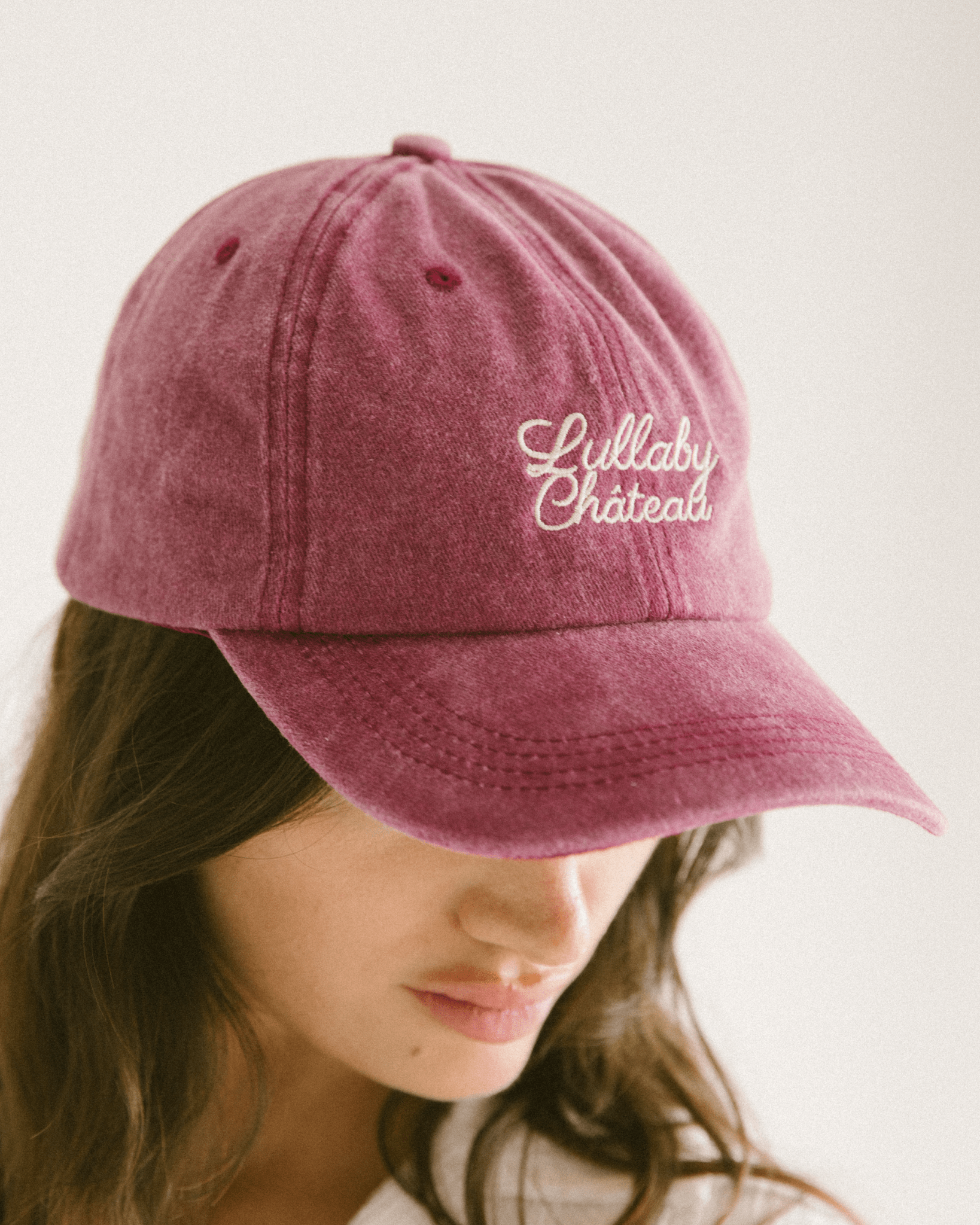 Person wearing a maroon cap with 'Lullaby Chateaux' text on a plain background