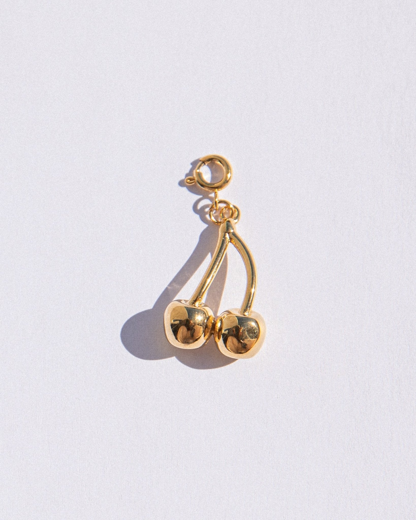 Gold cherry-shaped earring on a light gray background