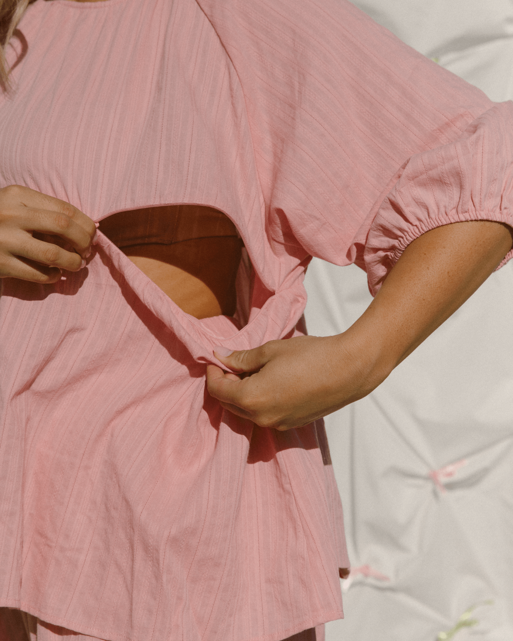 Woman wearing pink trendy top with hidden breastfeeding zippers.