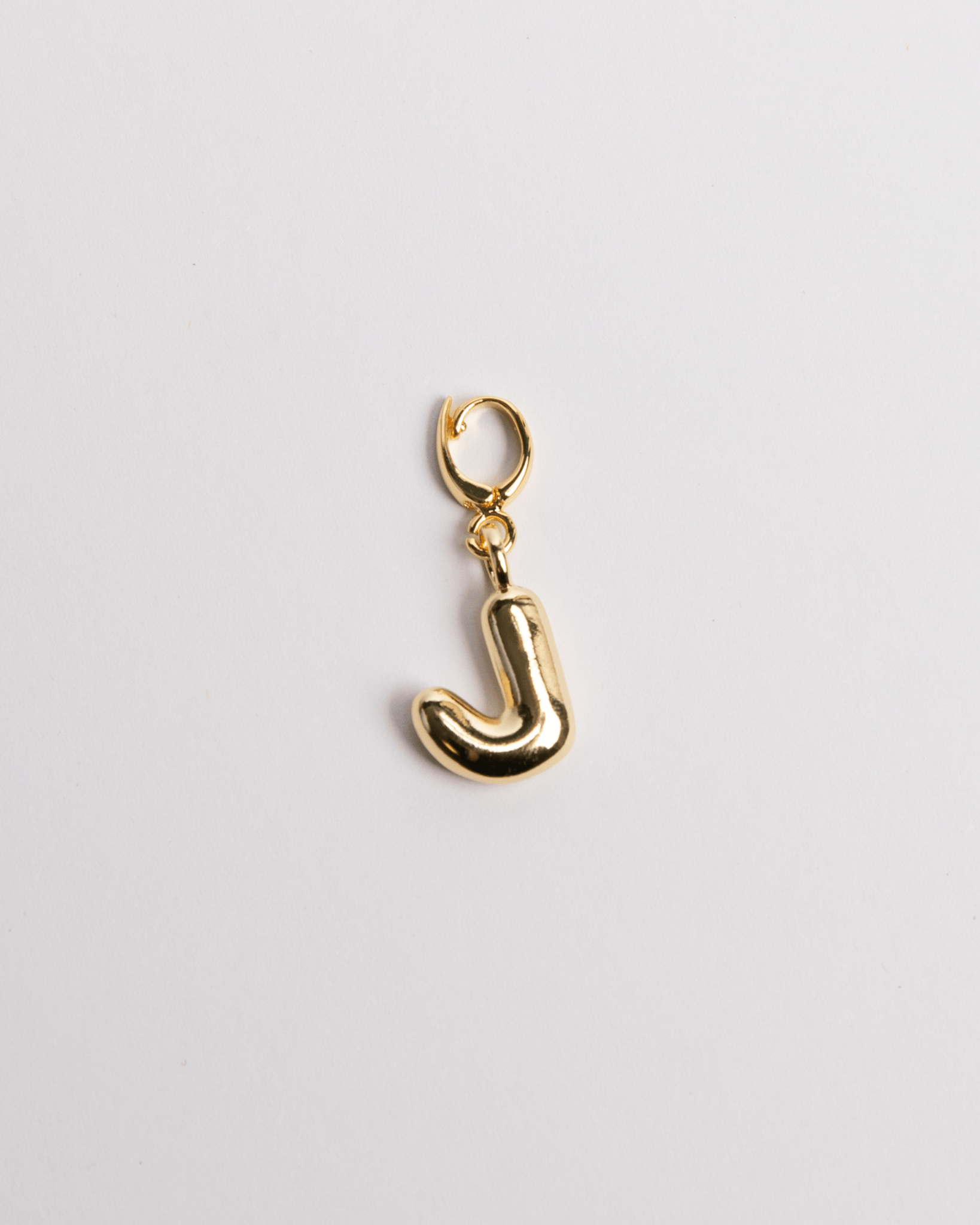 A gold-plated stainless steel charm in the shape of the letter J with a secure clasp on a white background.