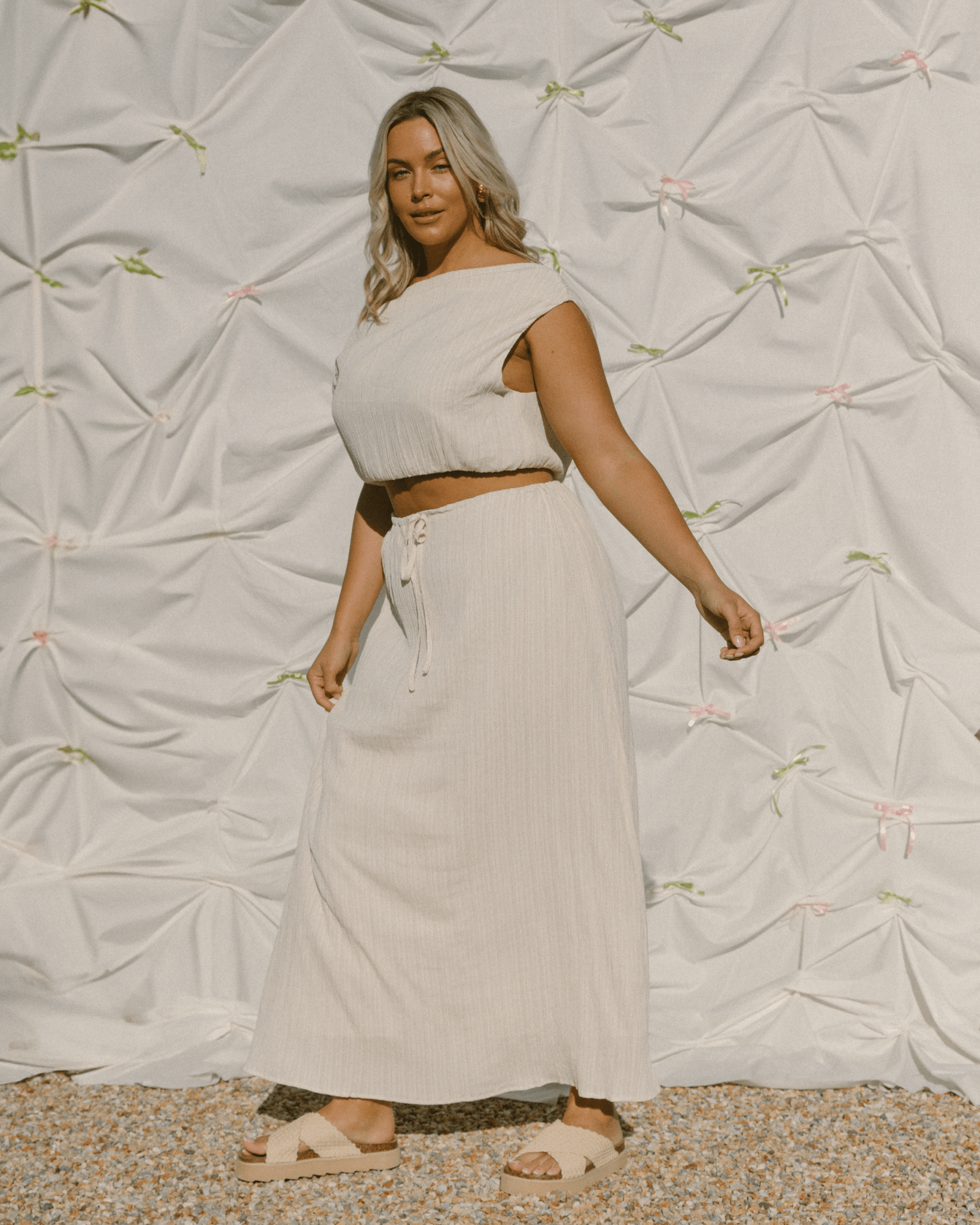 Woman wearing cream coloured crop top with boat neck and high-waisted drawstring skirt.