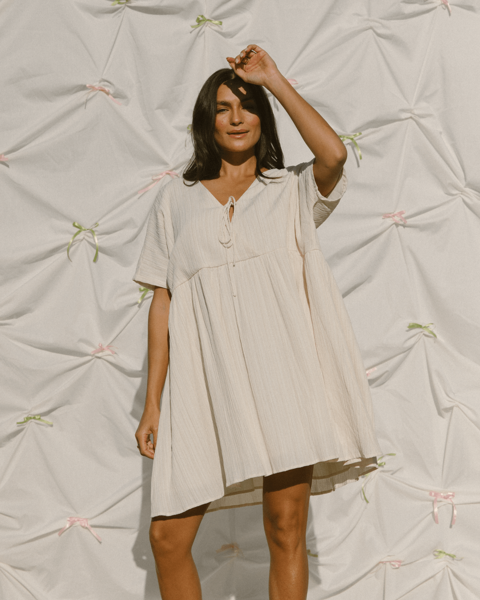 Woman wearing a summer mini dress in a light cream colour that has a wide-oversized deisng.