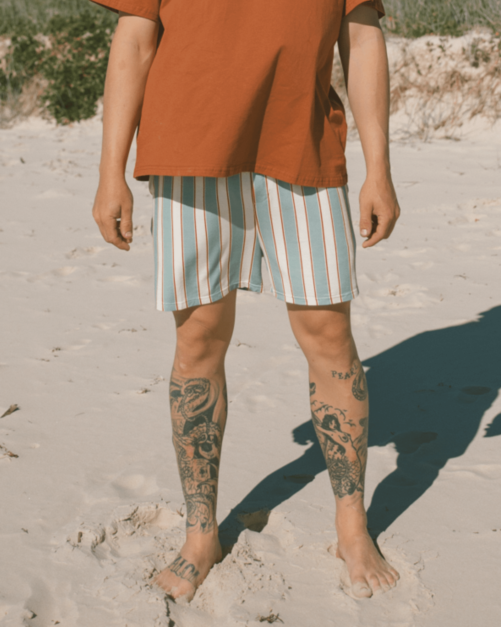 Man at beach wearing rust t-shirt and striped boxer shorts.