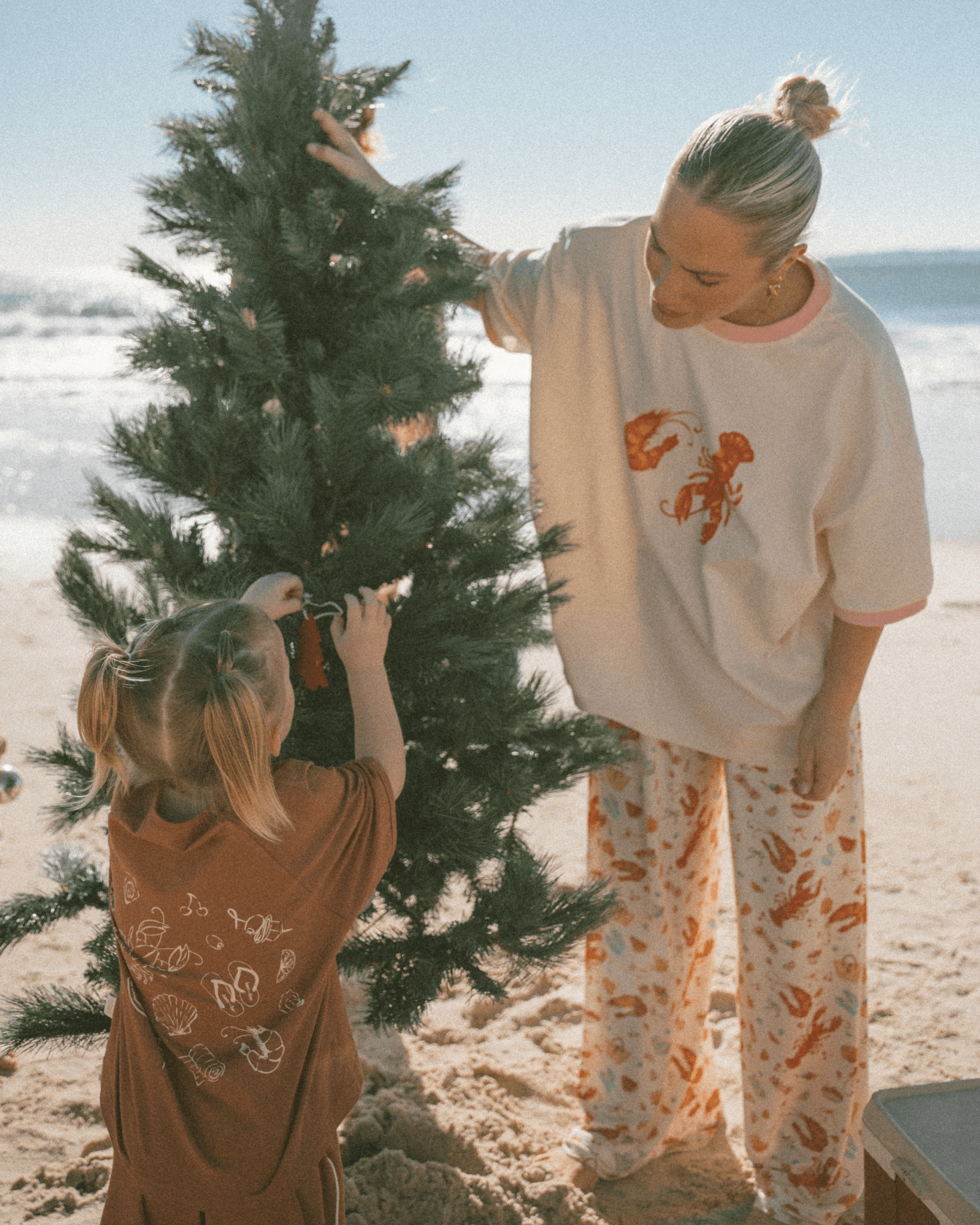 Mother & daughter decorating a christmas tree in matching australian christmas designed loungewear.