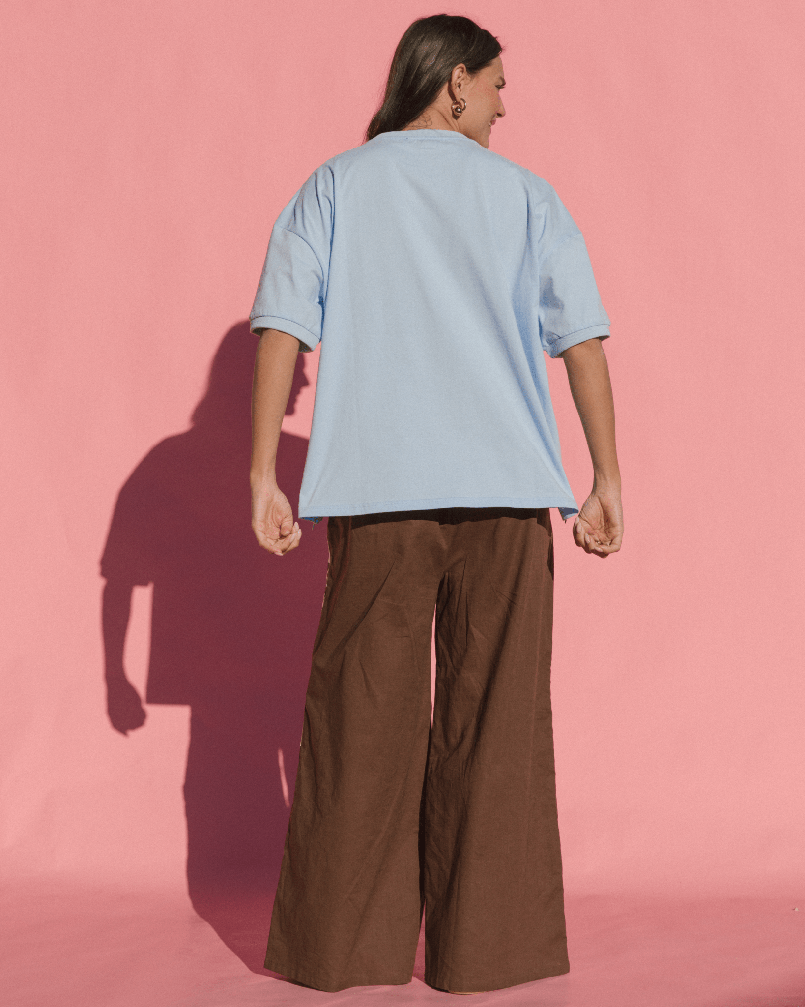 Person wearing a light blue shirt and brown pants against a pink background