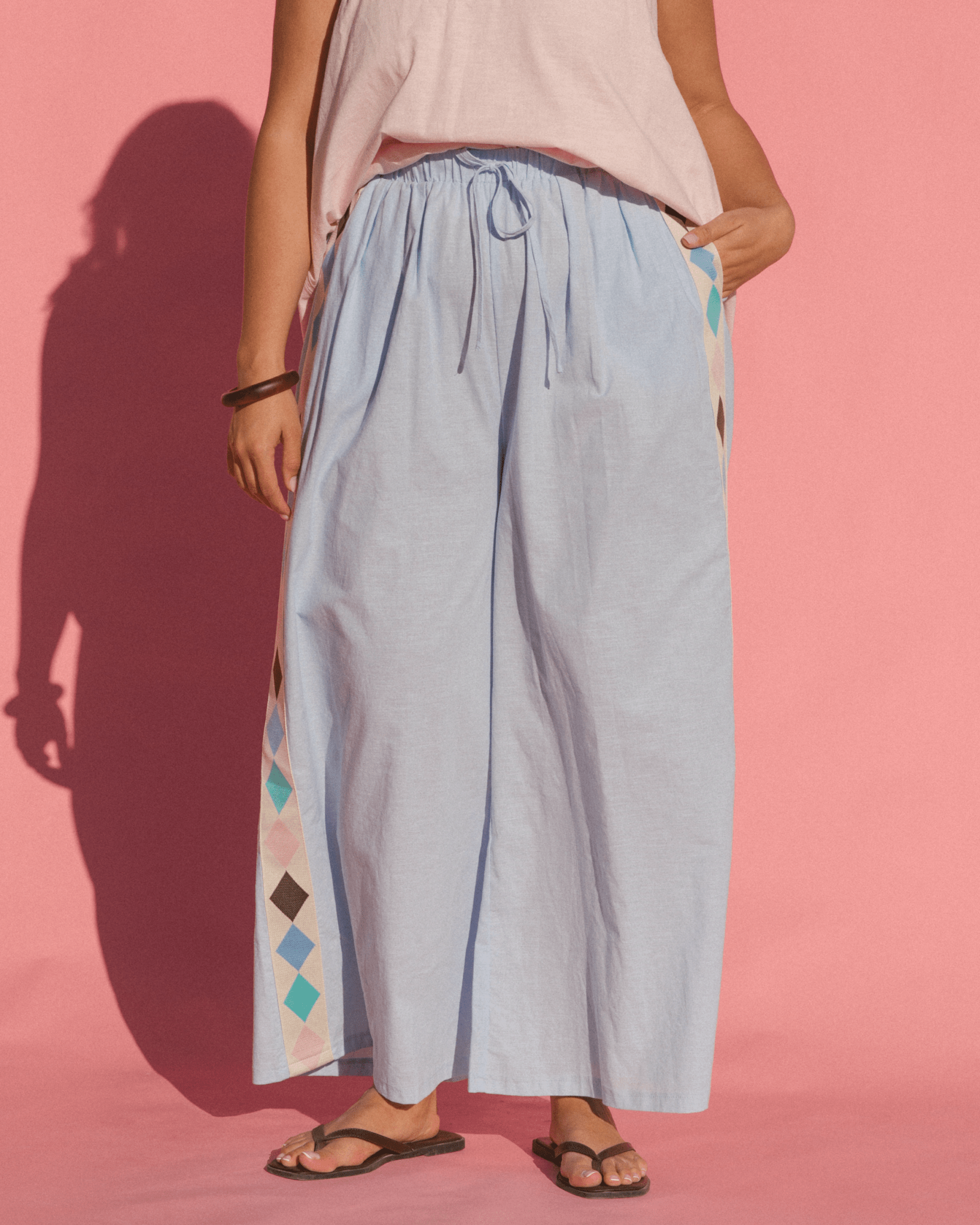 Close up of women wearing long pale blue wide legged cotton pants with multicoloured diamonds down the side-seam