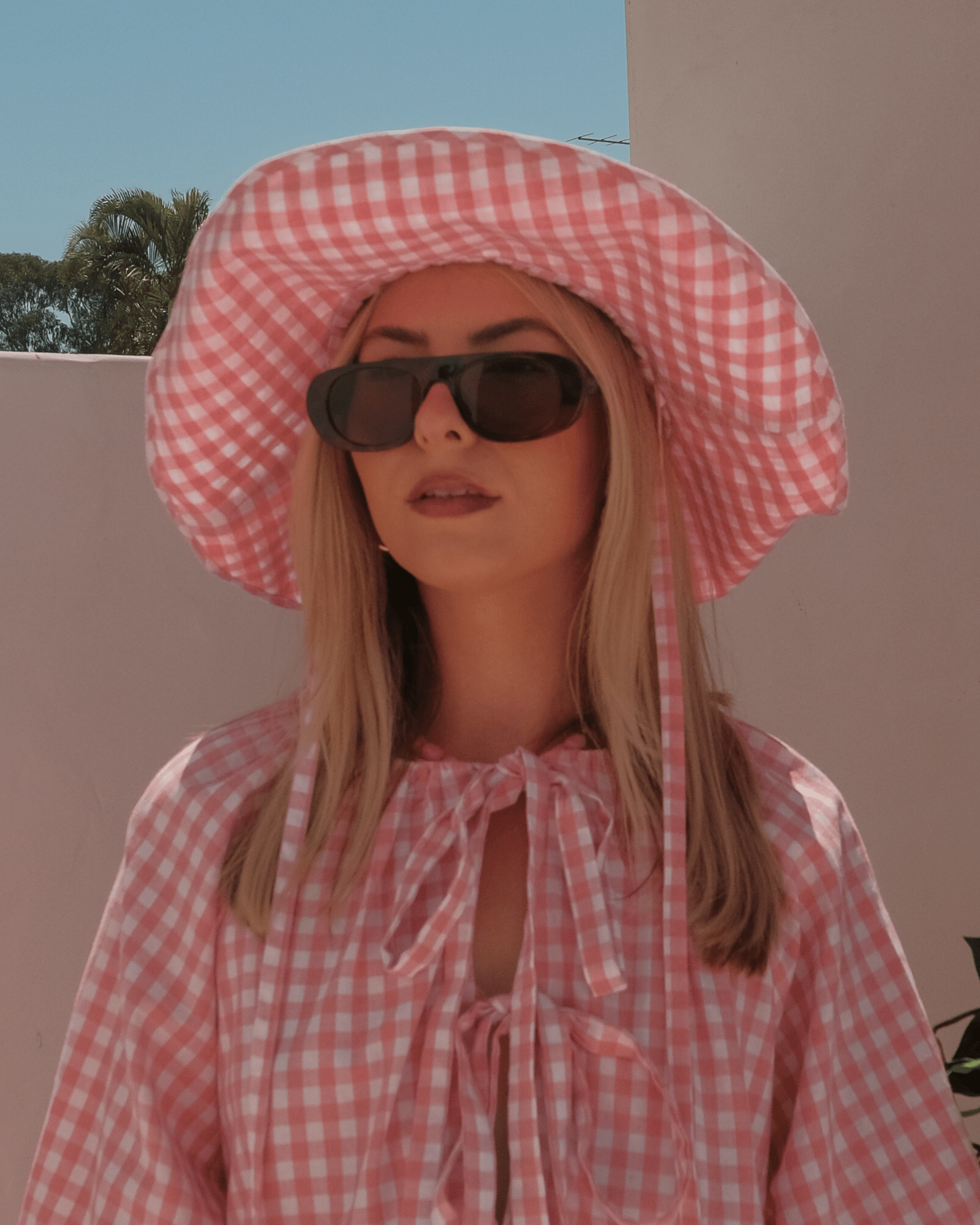 Woman wearing a spring outfit with pink gingham bow top and matching cotton wide-brimmed hat that has adjustable ties.