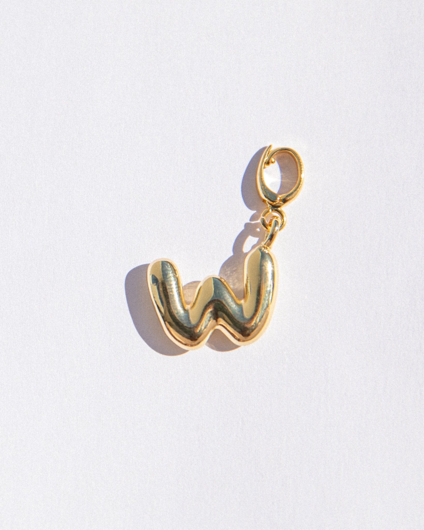 Gold charm shaped like the letter 'W' on a light gray background