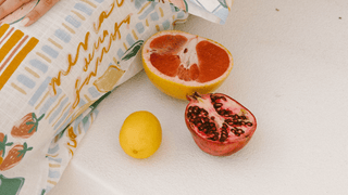 An arrangement of fruit including a lemon, pomegranate, grapefruit, while a printed pants in showing