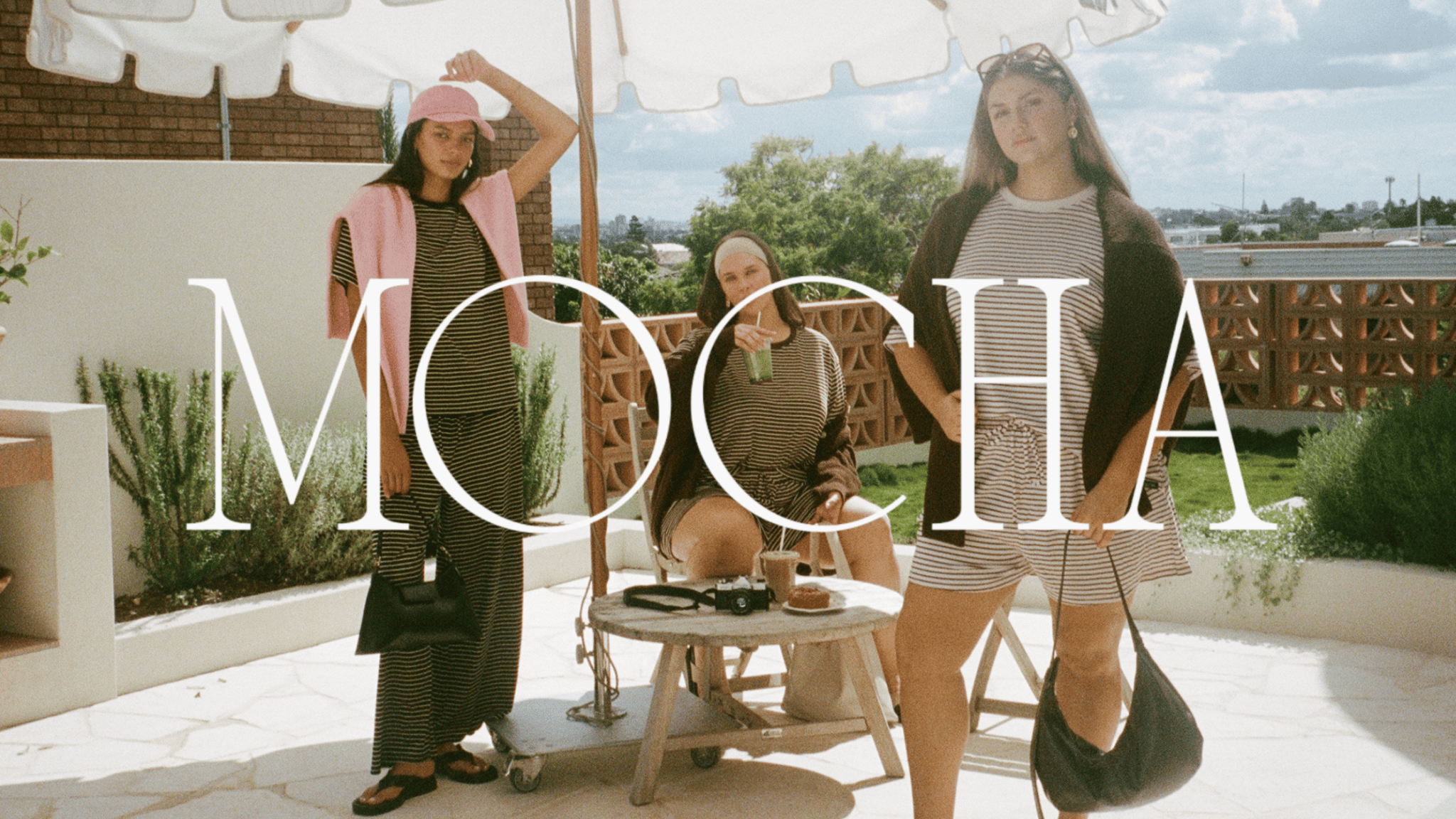 three girls in floral autumn outfits from the lullaby club merlot bloom collection wine colour set, gold vest, floral pants, florla set, headband drinking wine in green marble bend rattan chair and crazy pave tile kitchen 