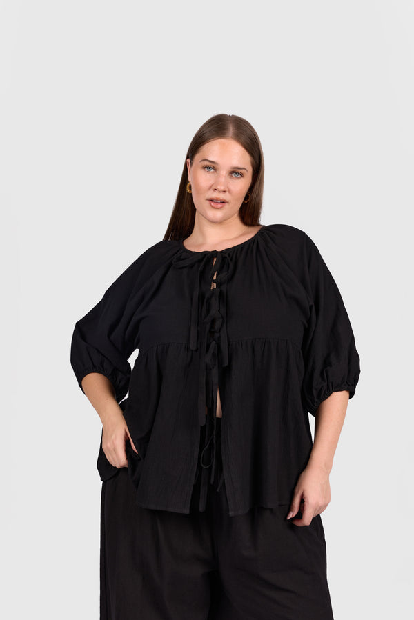 Woman wearing black tie up peplem style shirt. 