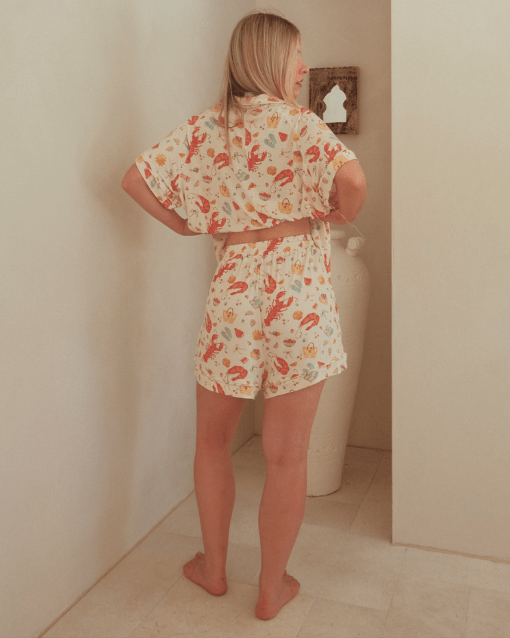 Woman wearing a collared summer, short sleeved, pj shirt and elastic band & relaxed-fit pj shorts in a Christmas print.