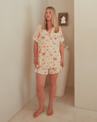 Woman wearing a pattern pajama set standing against a plain wall.