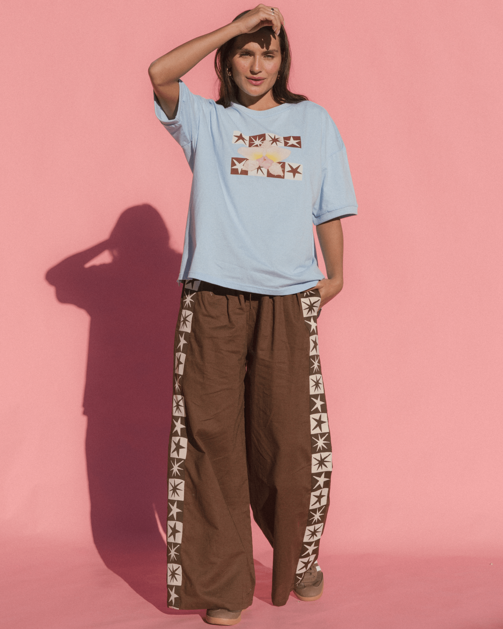 Woman wearing a light blue t-shirt and brown pants with star patterns on a pink background